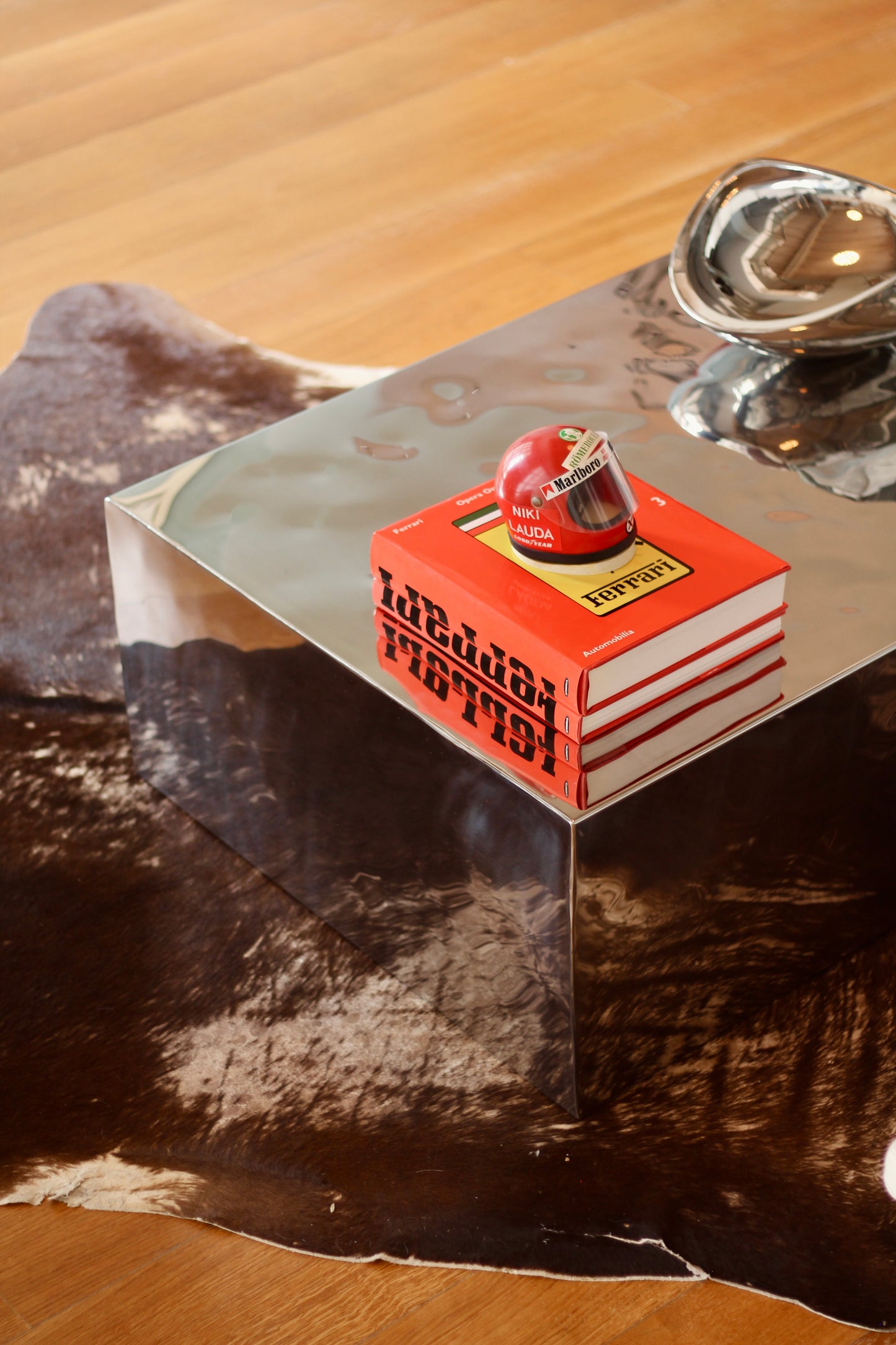 A stack of red and white books with a small red football helmet on top, placed on a reflective silver pedestal over a cowhide rug on a wooden floor.