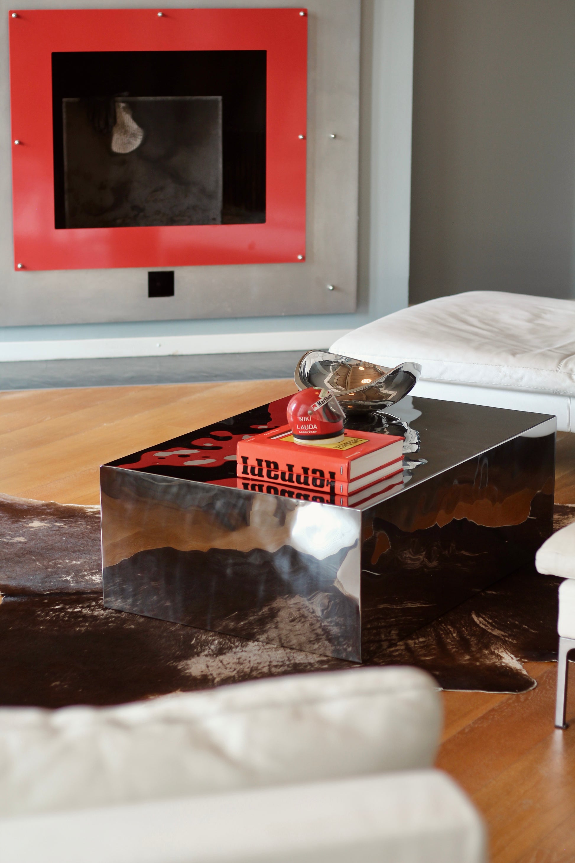 A modern rectangular coffee table with a glossy mirrored finish, styled with books and a decorative bowl in a living room setting.