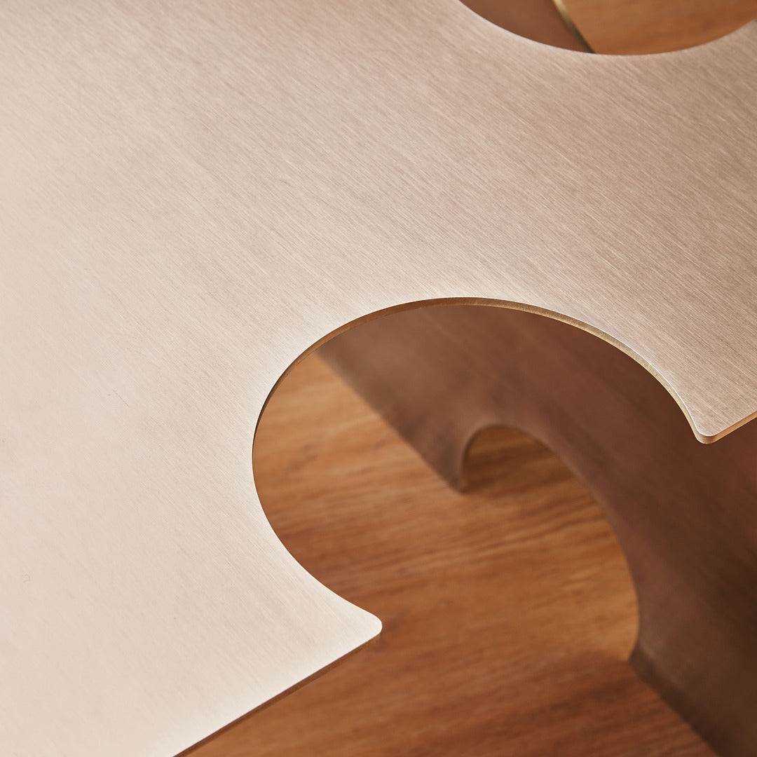 Artistic close-up of the “Puzzle Table” by Veliento — brushed stainless steel surface reflecting warm studio light and subtle color gradients.