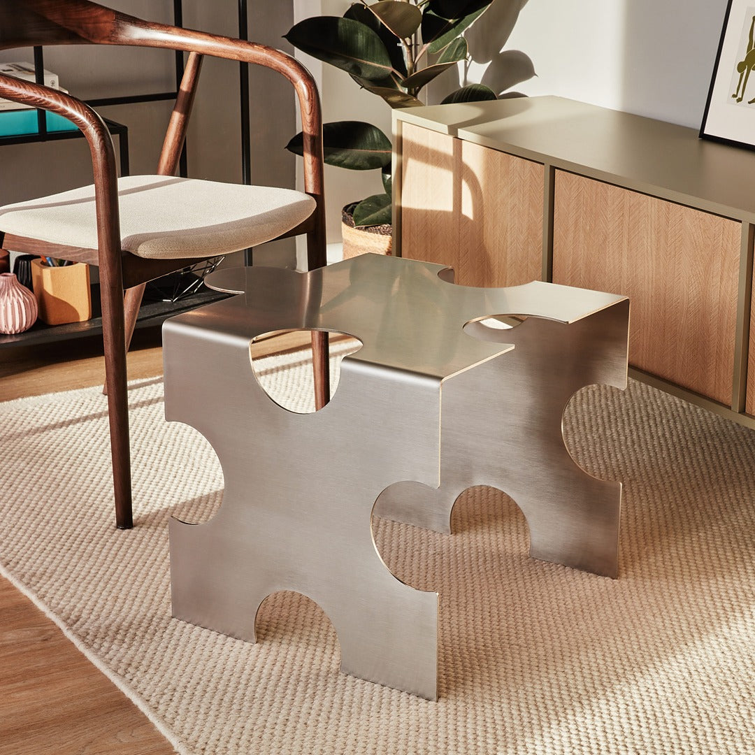 “Puzzle Table” by Veliento — brushed stainless steel side table styled in a warm European interior with modern wooden furniture and natural light.