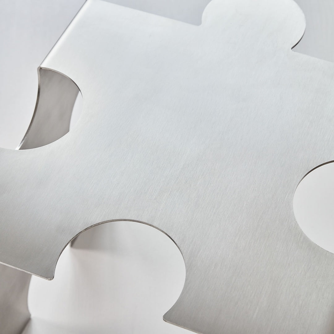 Top view detail of the “Puzzle Table” by Veliento — brushed stainless steel surface with soft reflections and sculptural edges.