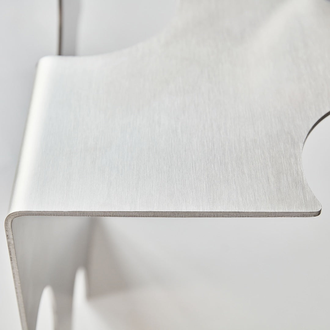 Minimal close-up of the “Puzzle Table” by Veliento — smooth brushed stainless steel surface with soft lighting and refined curvature.