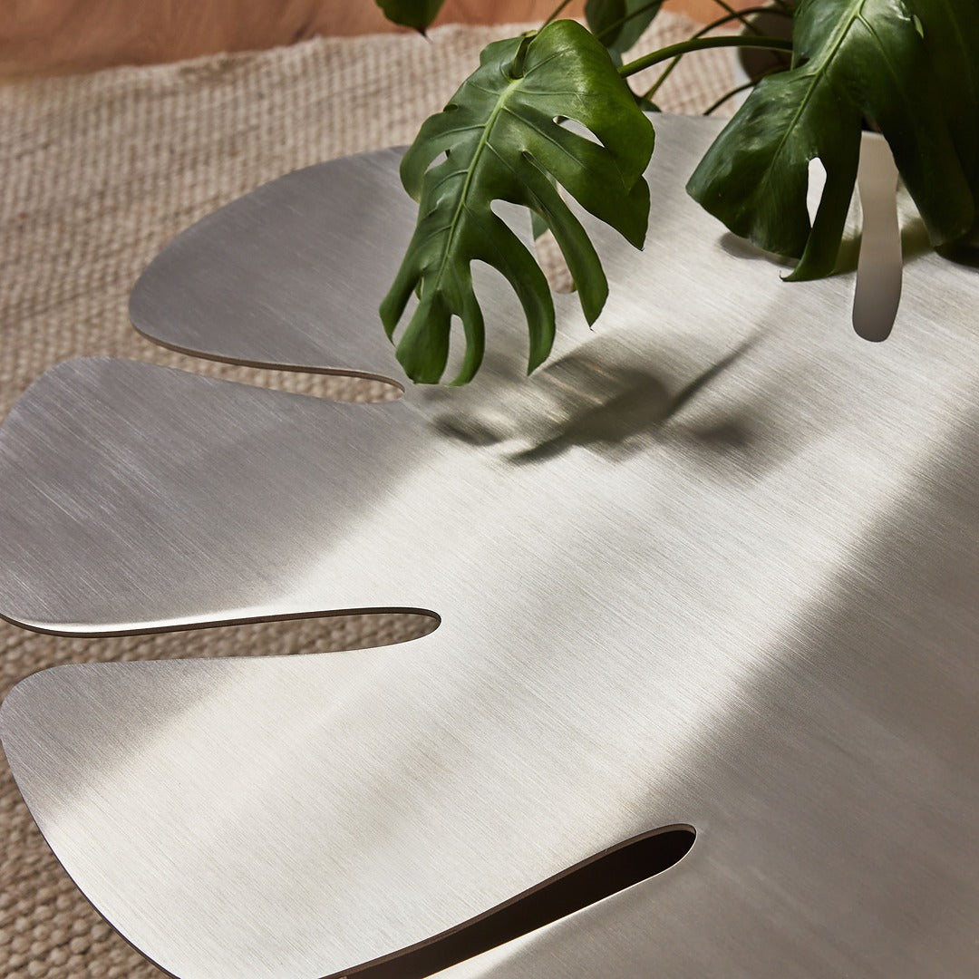 Stainless steel Monstera table styled with natural decor elements.