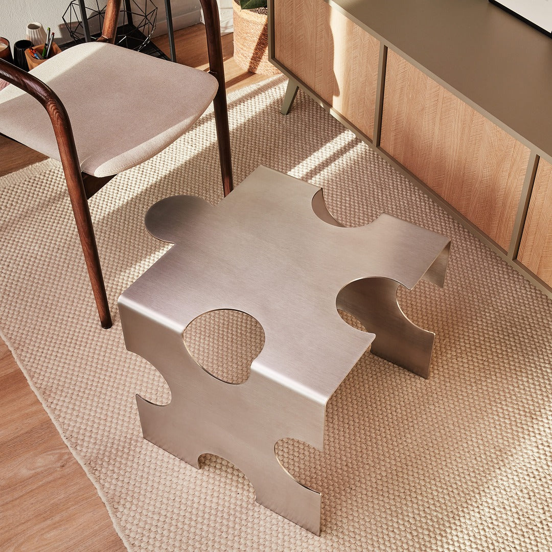 Modern metallic puzzle table in a room with wooden floor and chairs.