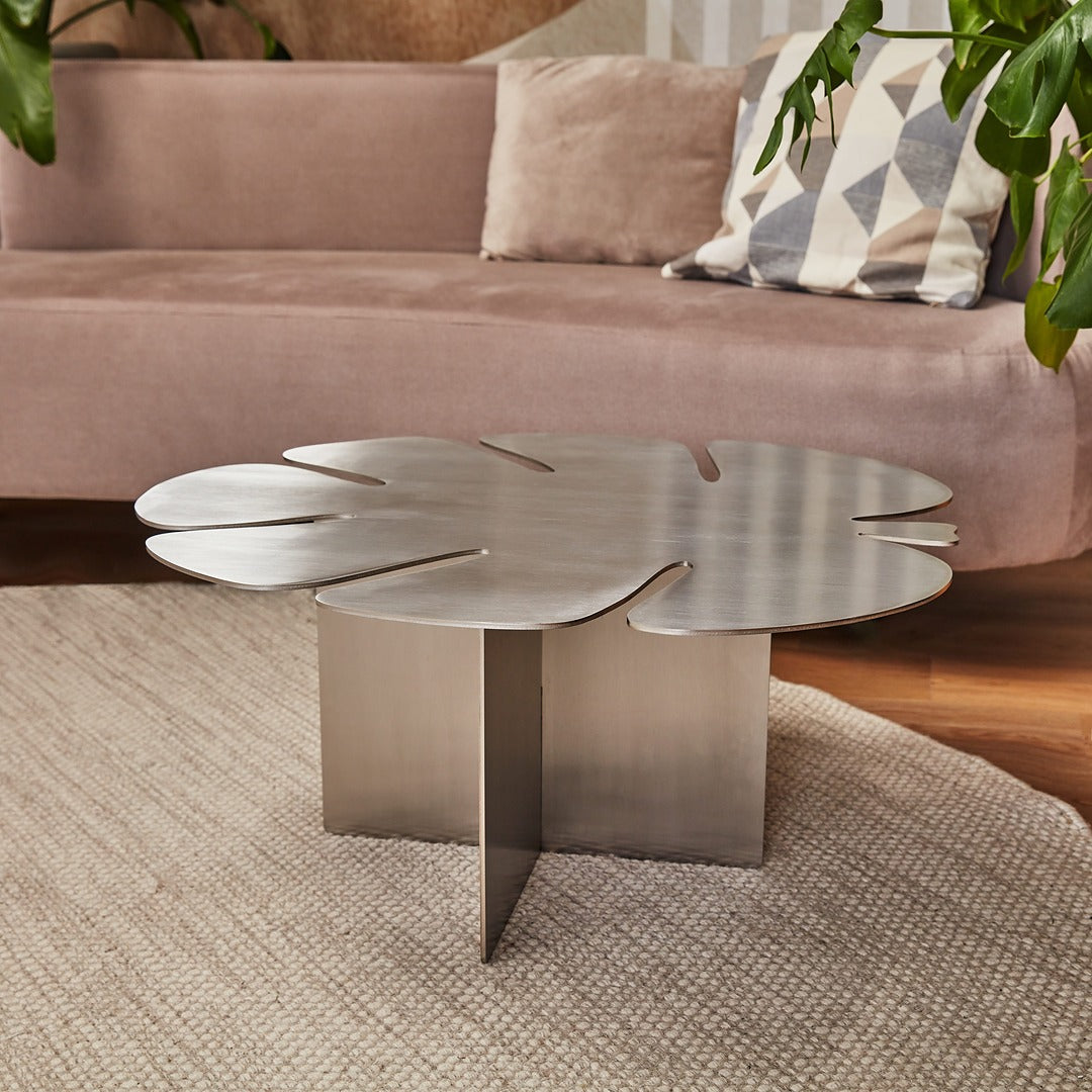 Designer stainless steel coffee table with Monstera leaf shape in stylish living room decor.