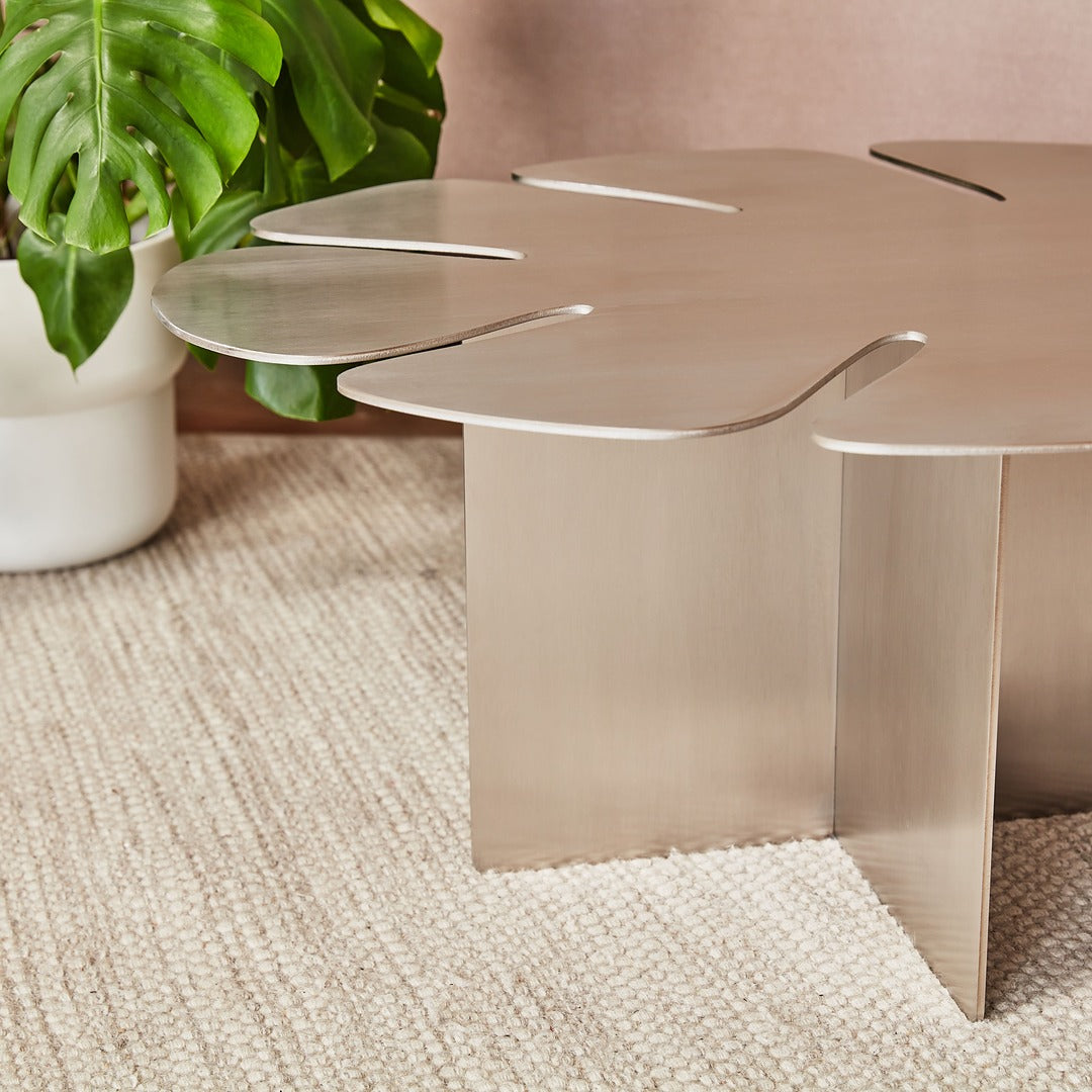 Modern metallic coffee table with leaf-like design on a textured surface