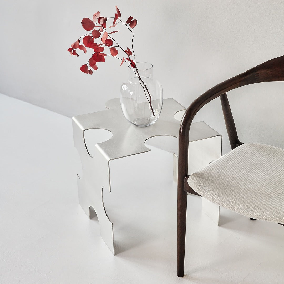 Modern white puzzle-style side table with a vase of red leaves and a chair on a light gray background