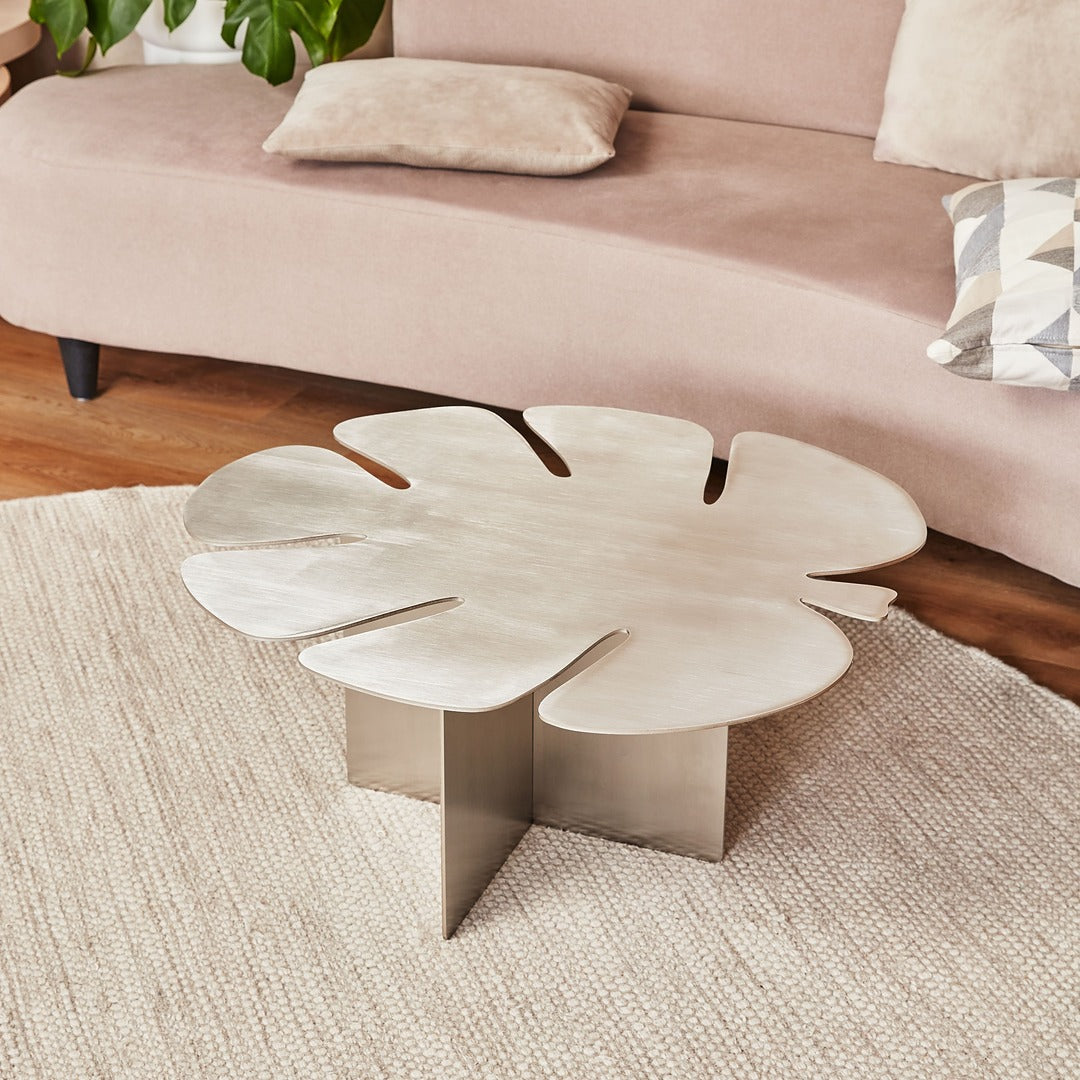 Sculptural brushed stainless steel Monstera coffee table in a modern minimal living room interior.
