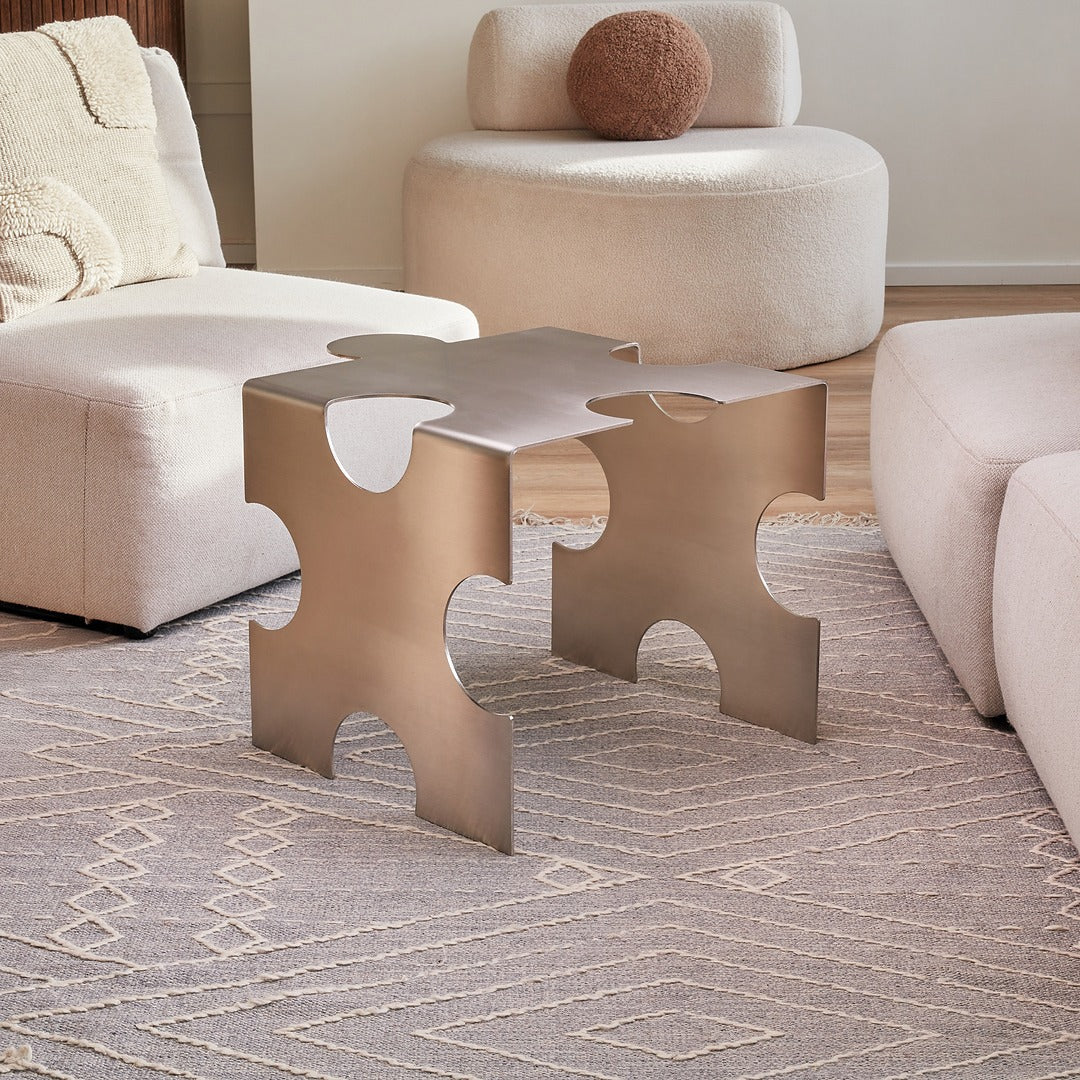 Modern metallic side table in a living room setting with beige furniture.